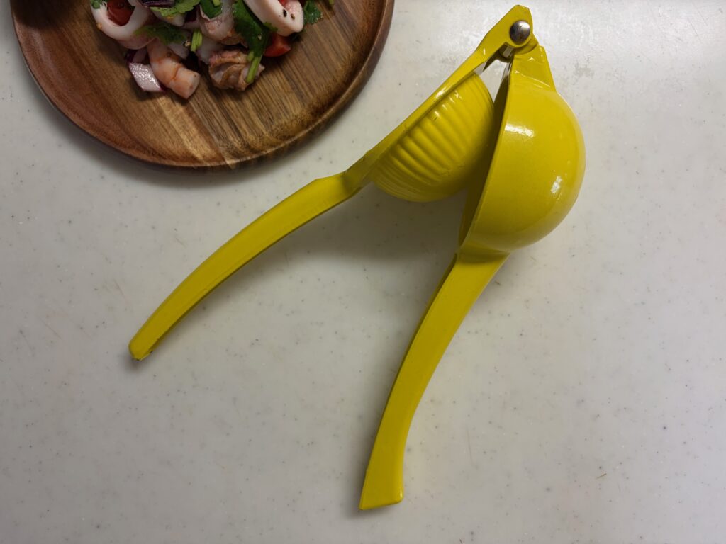 黄色いハンドジューサー(レモン絞り器)とセビーチェを盛った木皿