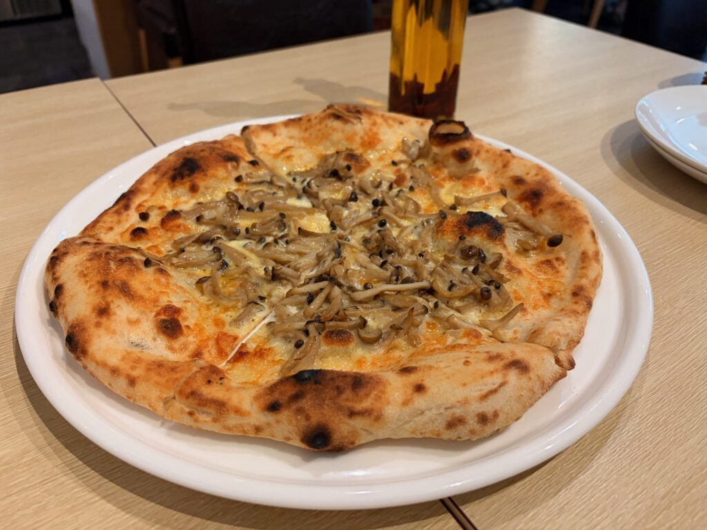 白い皿にのった、しめじやエリンギをのせた焼きたてのキノコのピザ