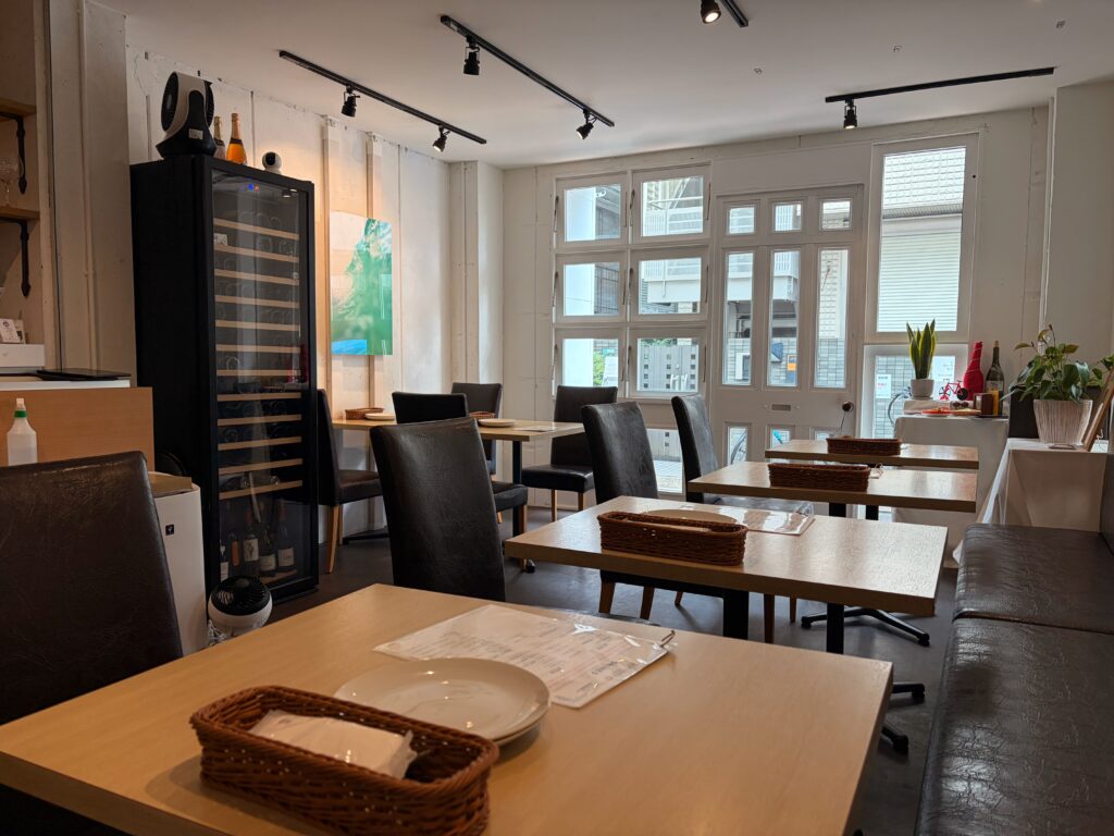白い壁と大きな窓、ワインセラーのあるPIZZA&WINE TAMURAの明るい店内