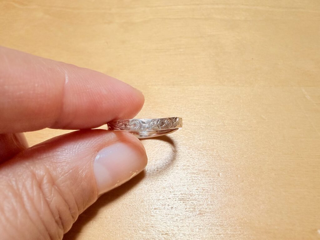 指先でシルバーの手彫りリングをつまんで持っている接写