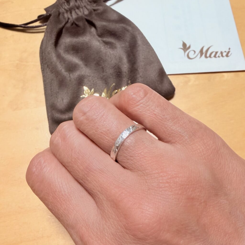 手の指にシルバーの手彫りリングをつけている様子、後ろにMaxiの巾着袋とブランドカード