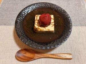 黒い丸皿にのった豆腐ともずくに梅干しを添えた軽食、木のスプーンを添えて