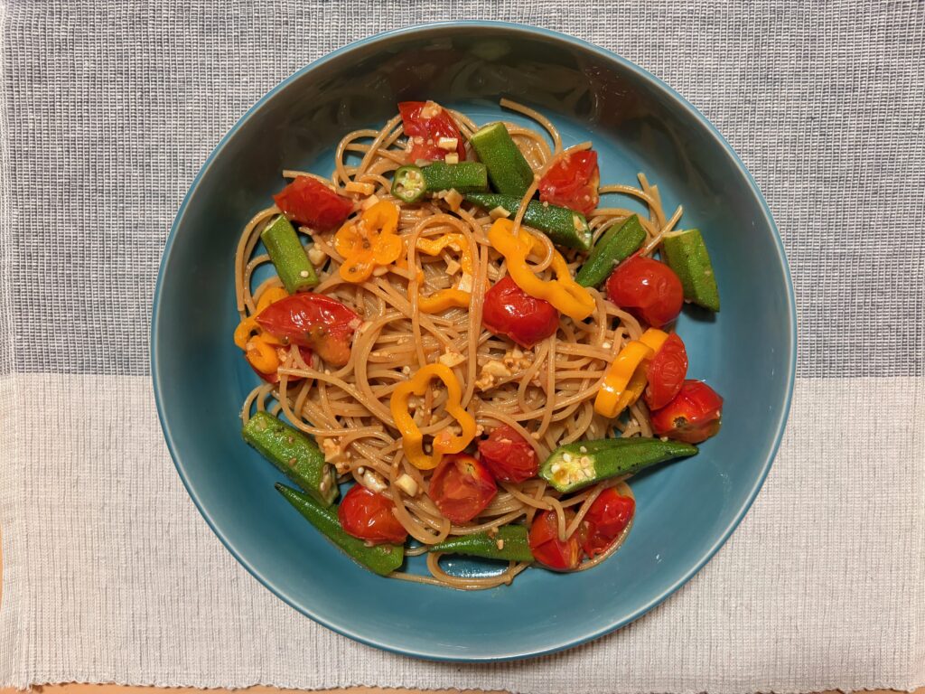 全粒粉スパゲティにミニトマト、オクラ、黄色パプリカを合わせたカラフル夏野菜パスタを青い皿に盛り付けた真上からの写真