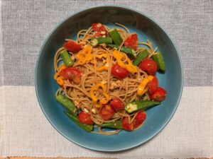 全粒粉スパゲティにミニトマト、オクラ、黄色パプリカを合わせたカラフル夏野菜パスタを青い皿に盛り付けた真上からの写真
